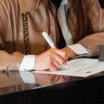 Close-up of a woman signing a document at a sleek reception counter, indoor setting.